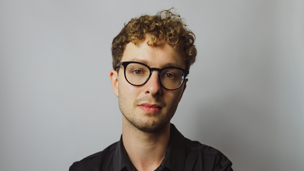 A man with short blonde hair, wearing glasses, smiling at the camera, wearing a black shirt.